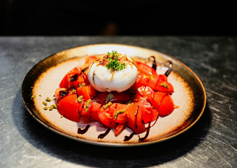 Burrata na komadima paradajza sa balzamikom i zelenim mrvicama, na keramičkom tanjiru