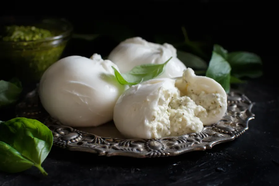 Burrata na srebrnom tanjiru sa bosiljkom, u pozadini pesto
